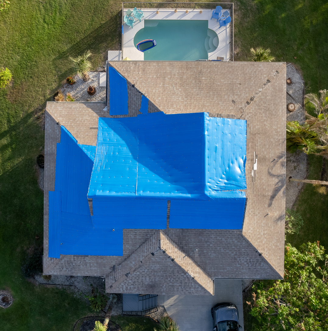 Storm-damaged house with a blue tarp covering the roof after a hurricane
