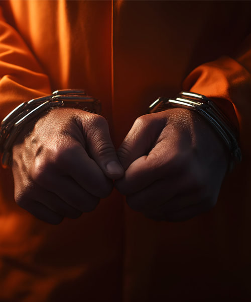 Inmate in orange uniform seated alone in a facility hallway, symbolizing conviction and incarceration