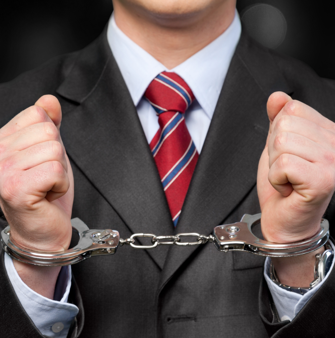 Man in a business suit wearing handcuffs, representing arrest for white collar crime